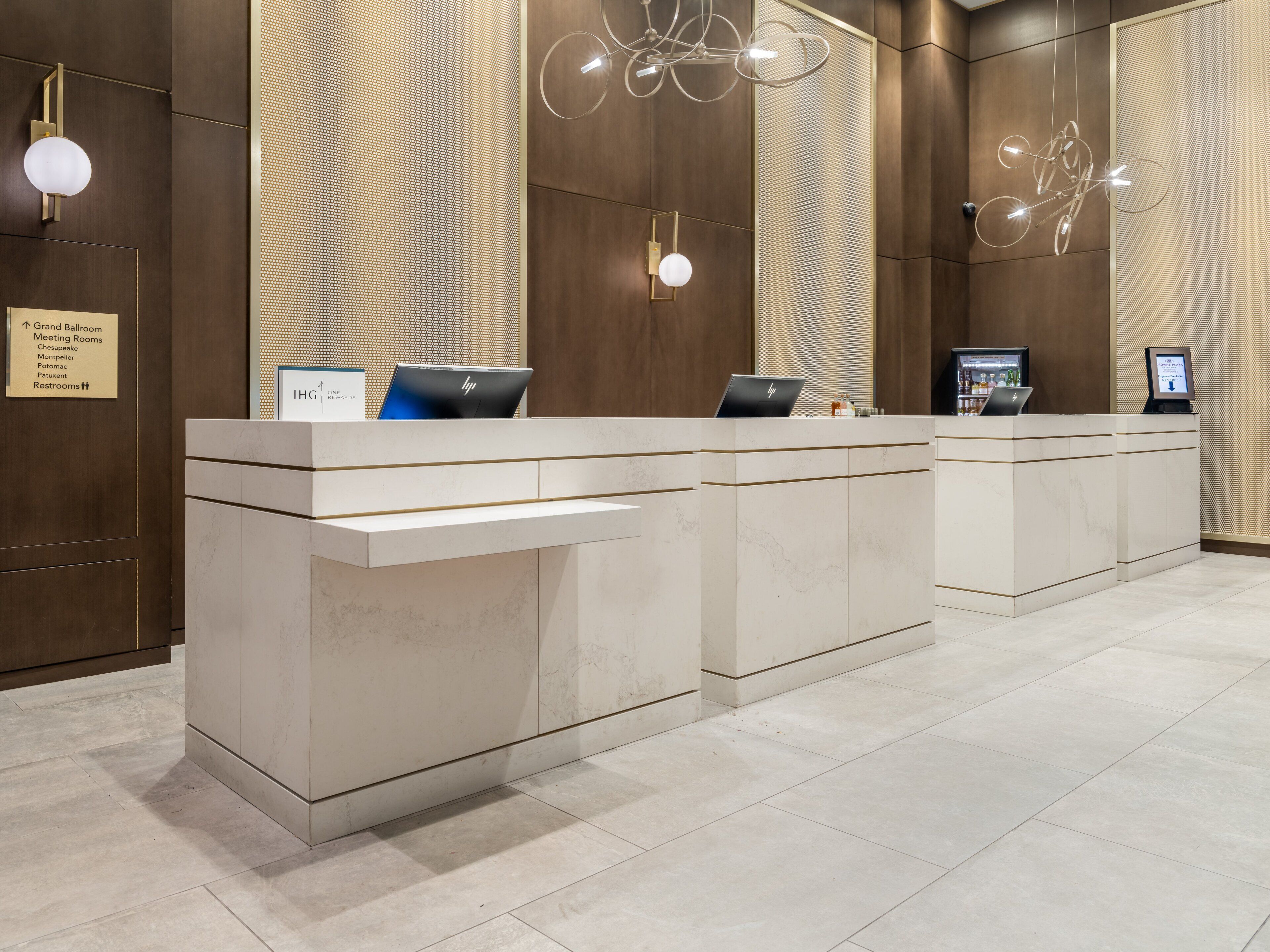 Un mostrador de recepción con dos portátiles HP, un cartel de IHG Rewards y señales indicativas para el Gran Salón de Baile, Salas de Reuniones y Baños.
