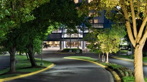 A well-lit entrance to a hotel with a modern building, a curved driveway, and surrounding greenery.