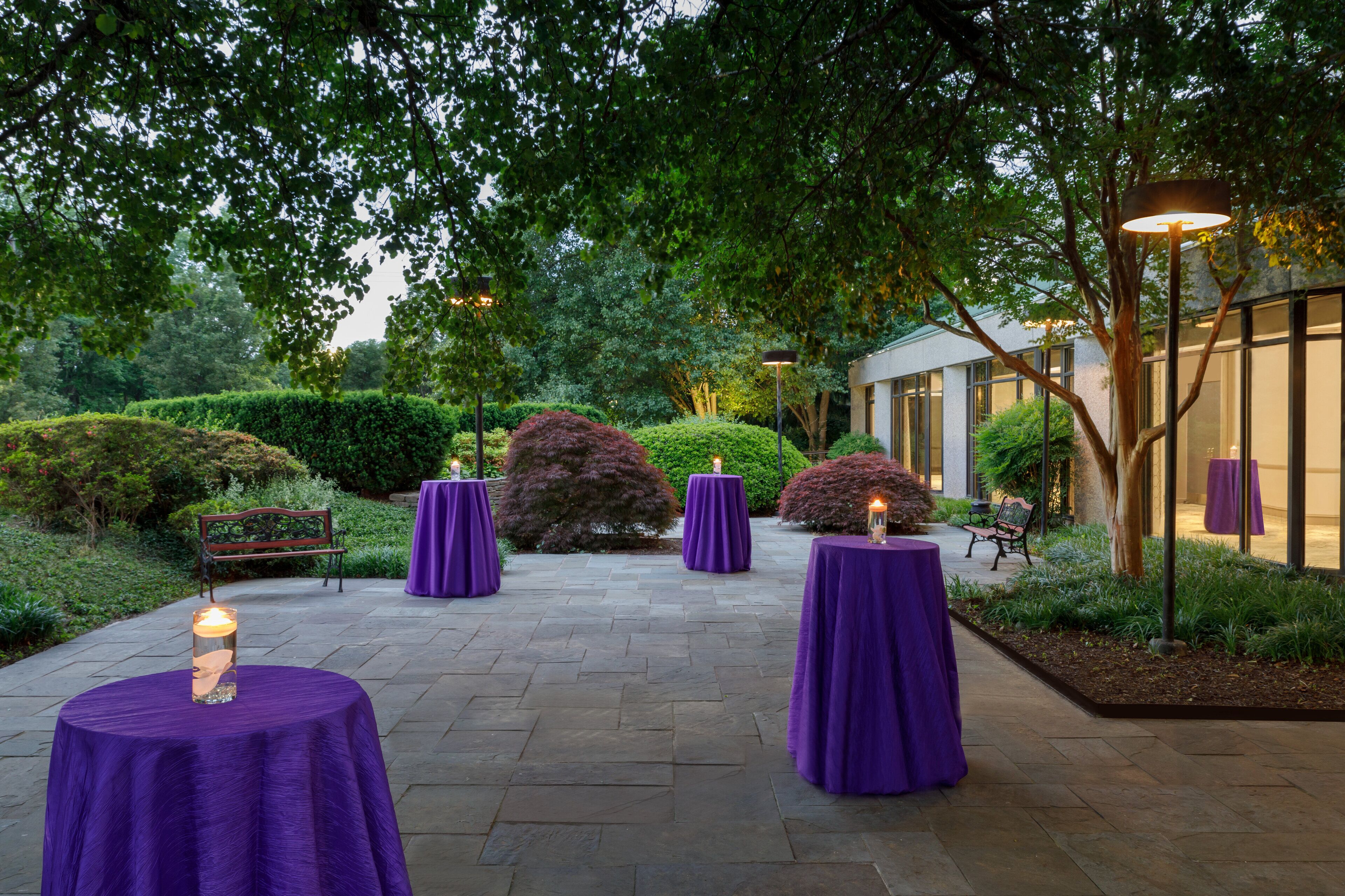 An outdoor patio area with stone flooring, surrounded by lush greenery and trees.