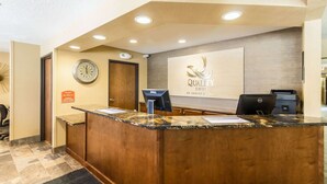 A hotel reception desk with a clock, a Dell monitor, and a sign that reads "Quality Inn by Choice Hotels".