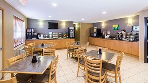 A hotel dining area with multiple tables and chairs, a coffee station, and a kitchen area with appliances.