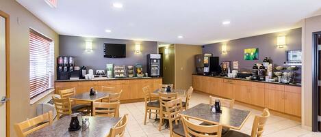 Un espace de restauration d’hôtel comprenant plusieurs tables et chaises, un coin café et une cuisine équipée.
