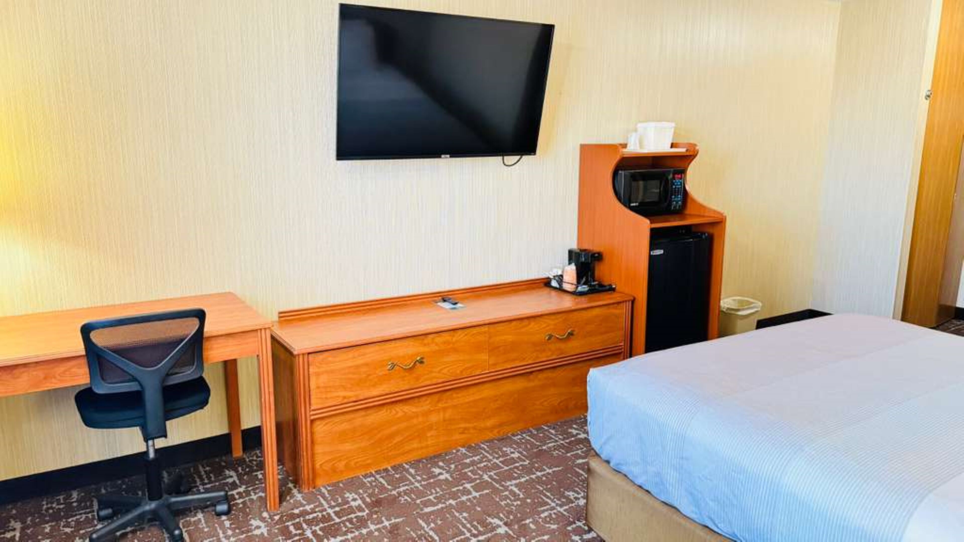 A hotel room with a bed, a desk with a chair, a television, a coffee maker, and a microwave.