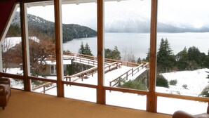 Habitación con ventanas amplias que ofrecen vistas a un lago, un paisaje nevado y una terraza de madera.