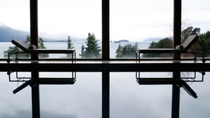 Una habitación con un ventanal grande con vista a un lago, dos sillas y una mesita.