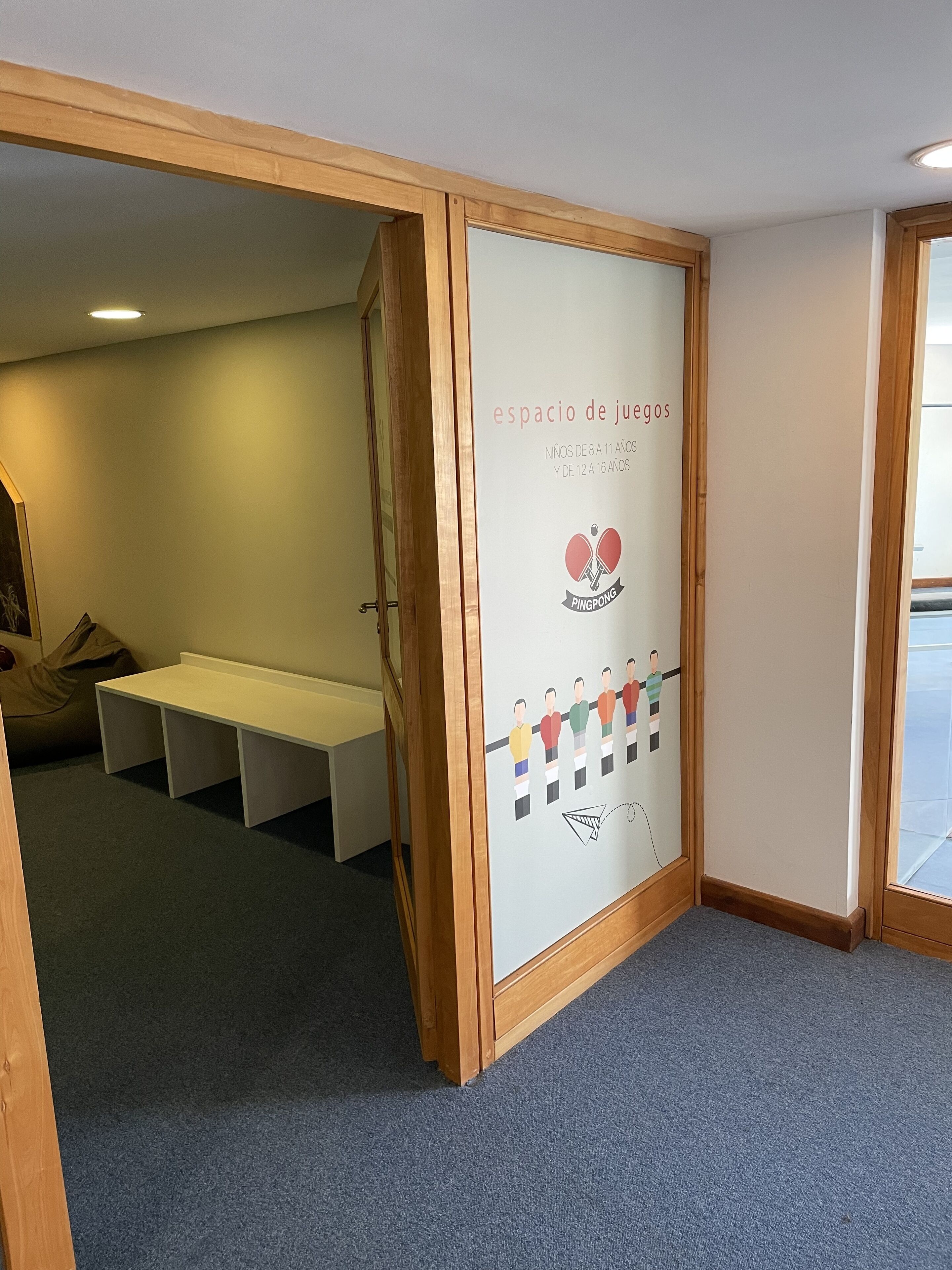 Zona infantil con un banco de madera y una pared con el logo de Ping Pong e indicación de que es un espacio para niños y adolescentes de 8 a 16 años.
