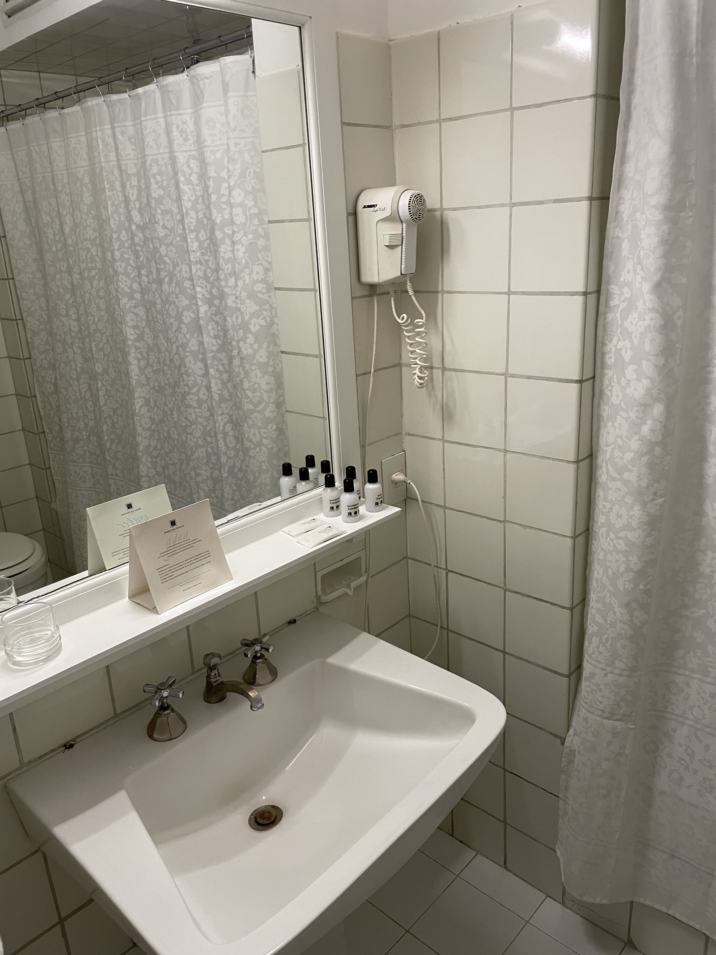 A bathroom with a white sink, mirror, and a hairdryer mounted on the wall.