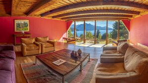 Un salón acogedor con techo de madera, ventanas grandes y vistas a las montañas.