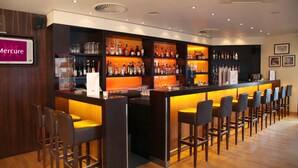 Zona de bar con varias estanterías llenas de botellas, taburetes y un cartel que dice "Mercure".