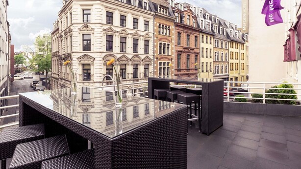 Terraza en la azotea con mobiliario de mimbre, vistas despejadas a edificios históricos y un letrero de hotel.