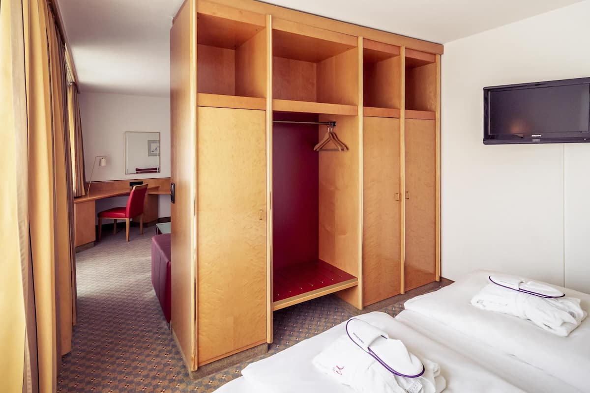Ein Hotelzimmer mit Holzschrank, Schreibtisch mit Stuhl, Fernseher und Bett mit Handtüchern.