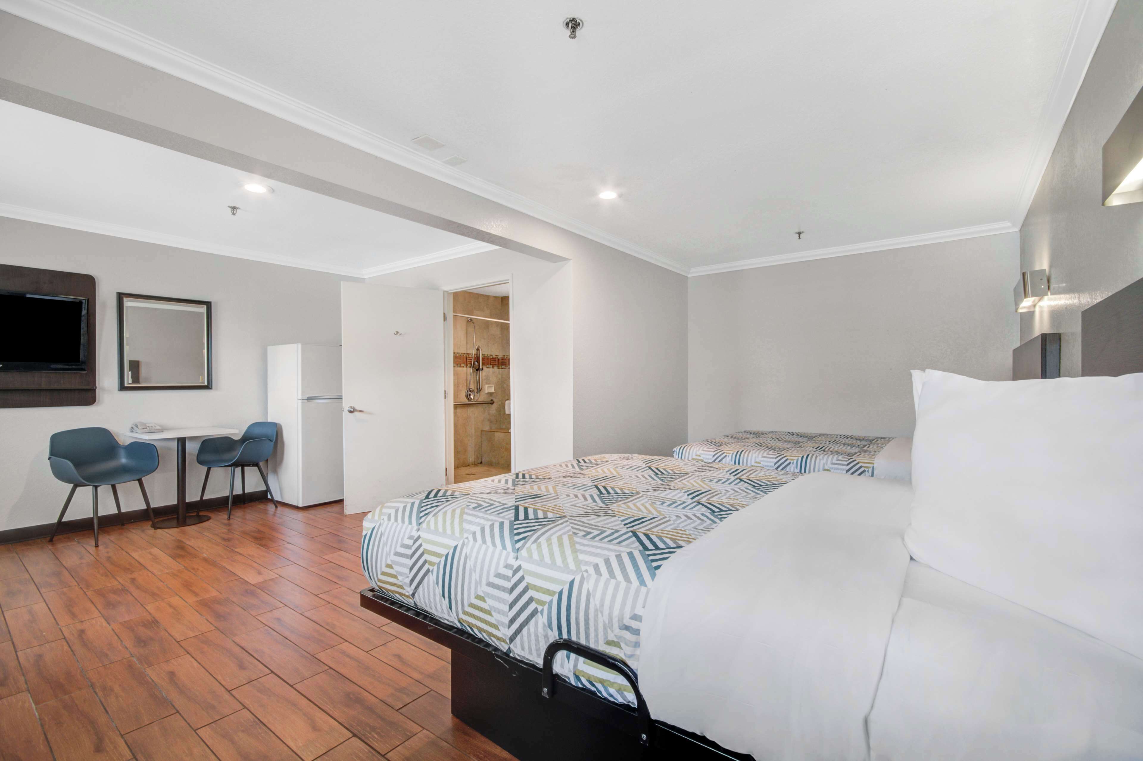 A modern hotel room with a bed, a desk with chairs, and a wardrobe.