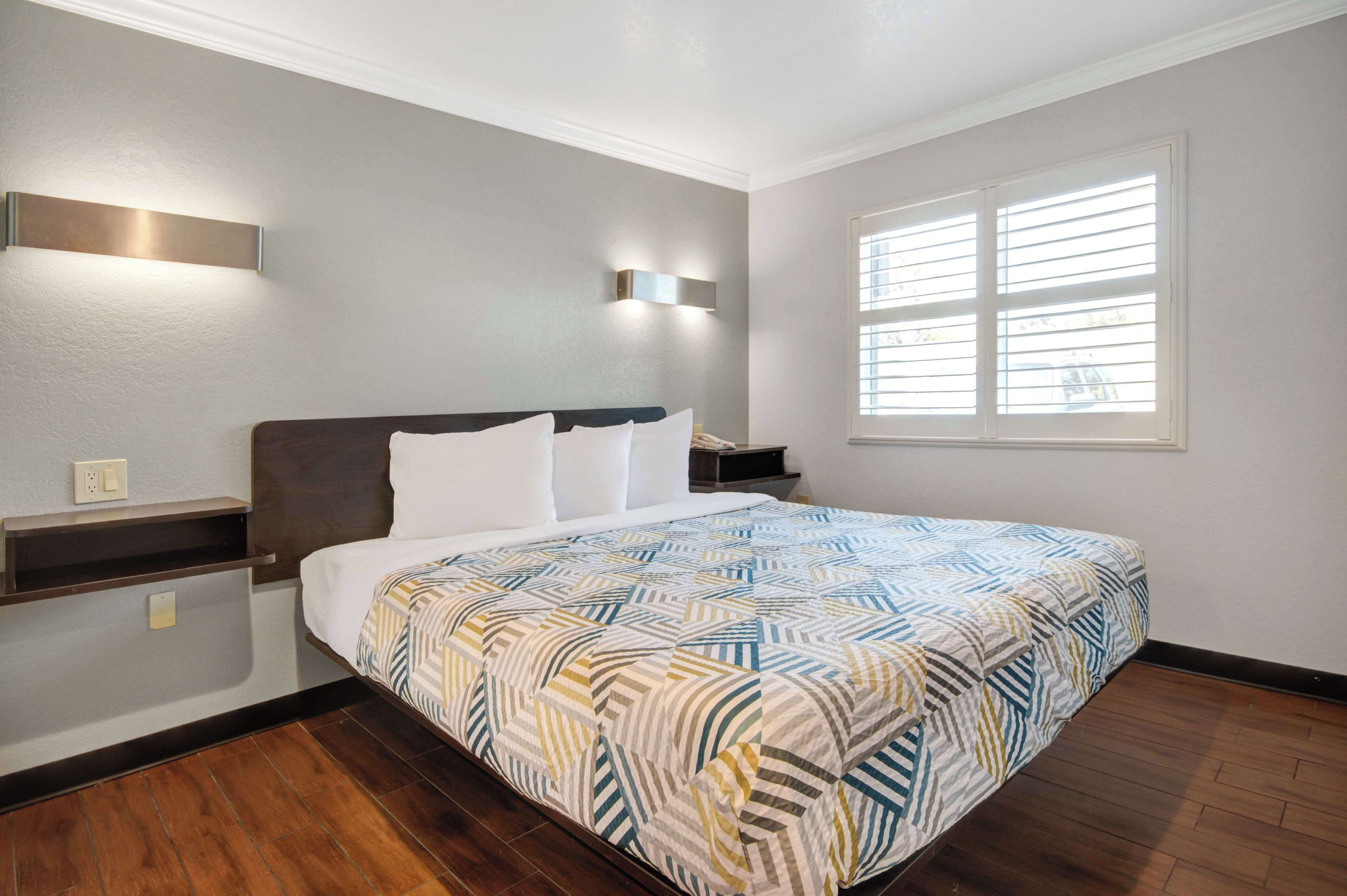 A hotel room with a large bed, a nightstand, a wall-mounted light, and a window with blinds.