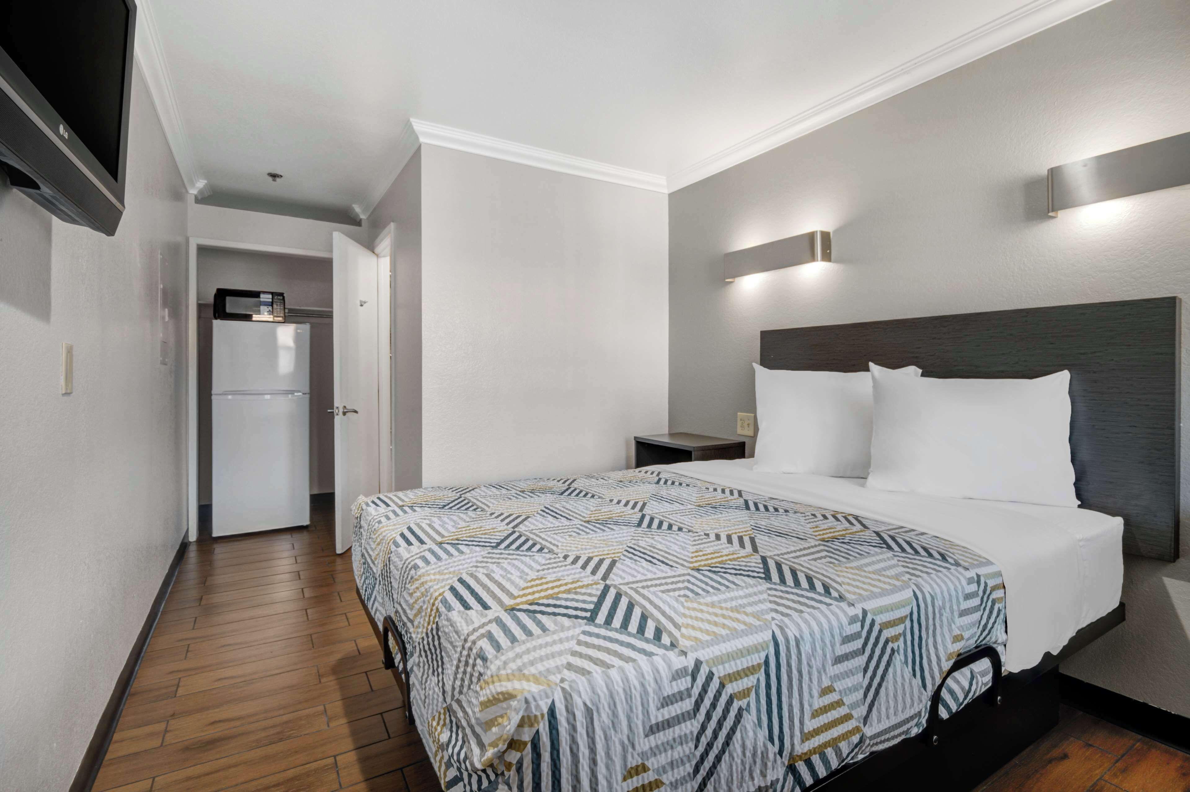 Una habitación de hotel con una cama, una mesita de noche, una lámpara de pared y un microondas en la esquina.