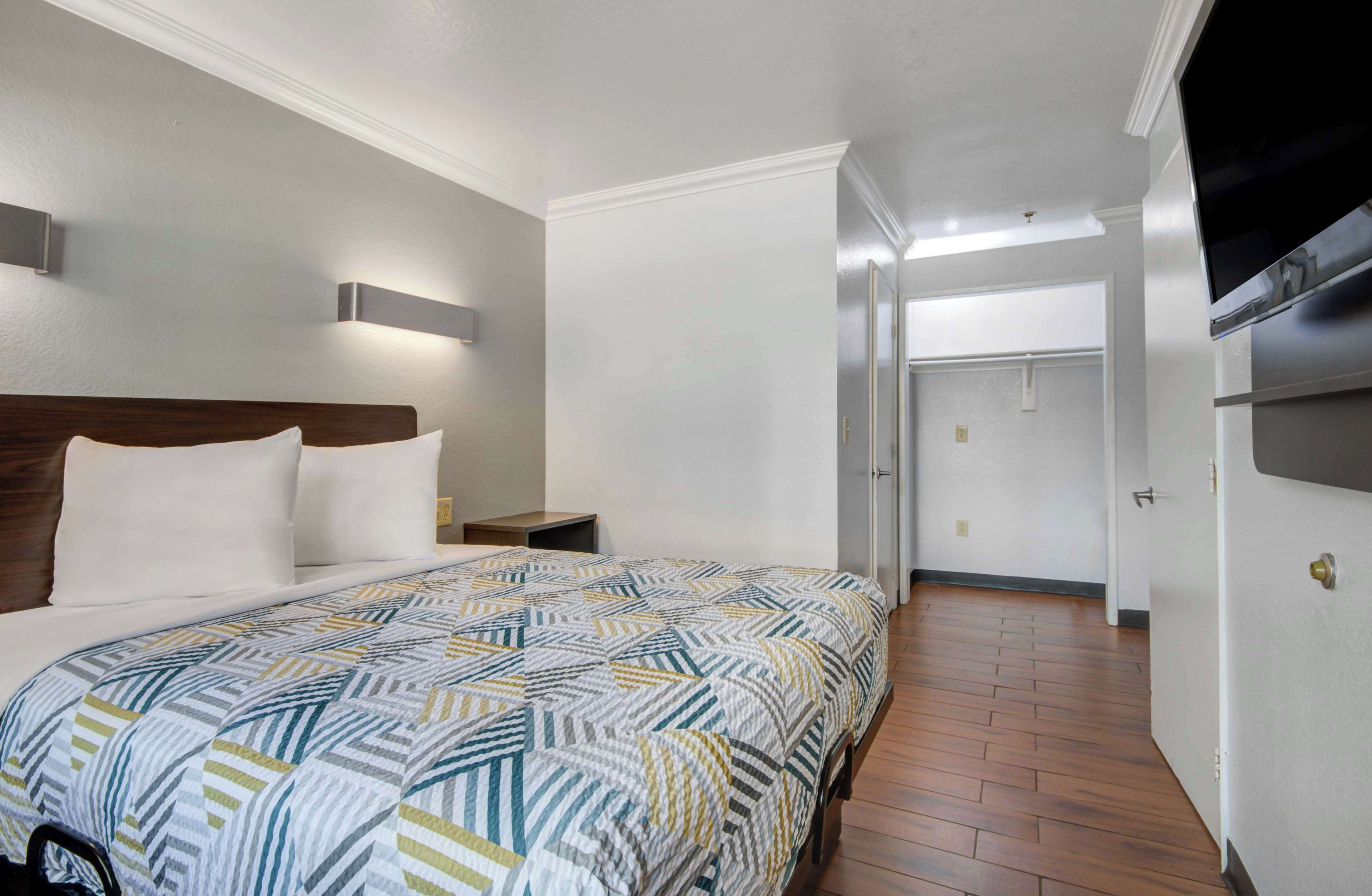 A hotel room with a large bed, a wooden headboard, a nightstand, and a wall-mounted TV.
