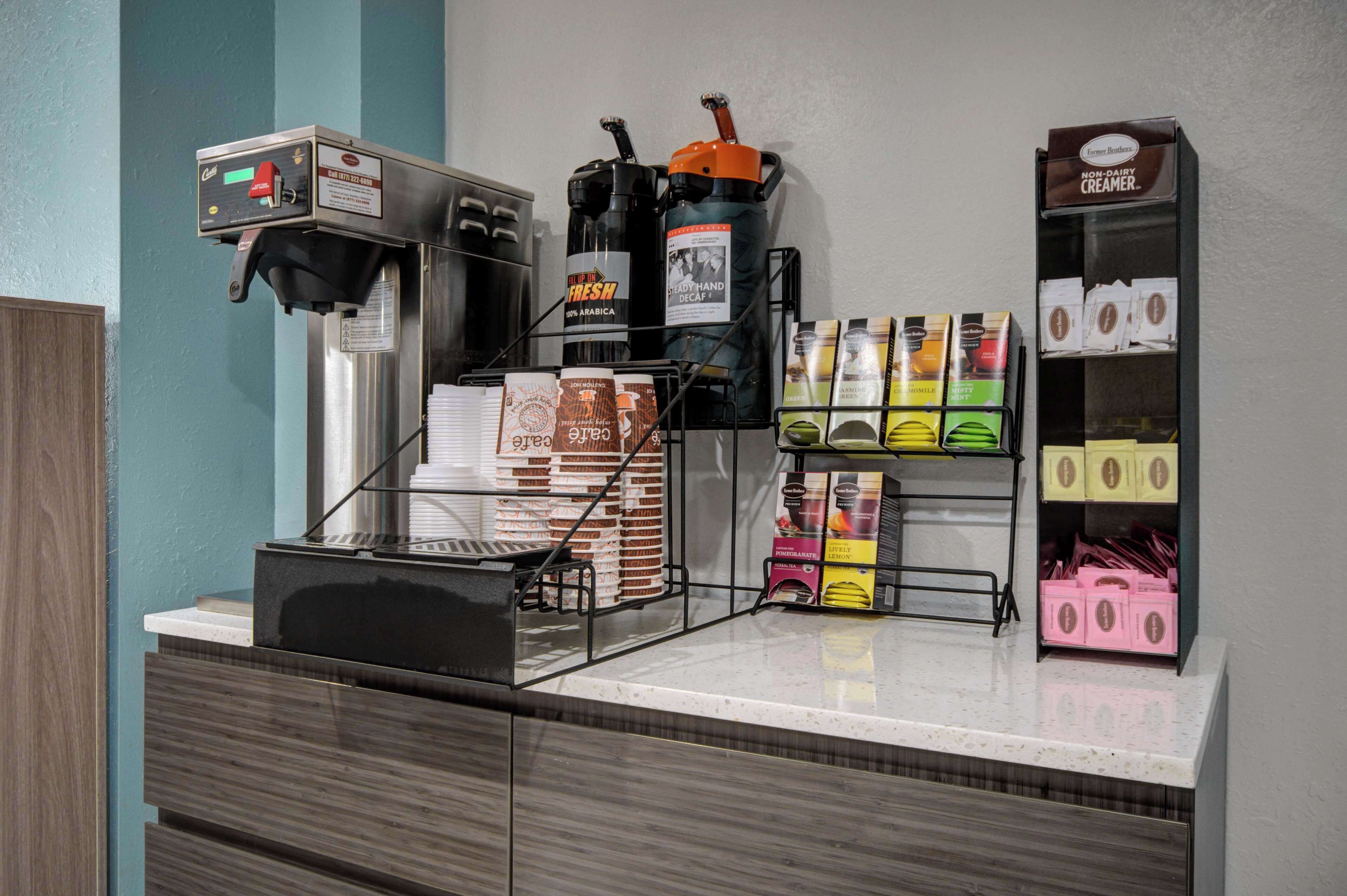 Un espace dédié au café, équipé d’une machine à café, d’une machine à expresso et de distributeurs de café. On y trouve des piles de tasses à café et des boîtes de capsules de café.