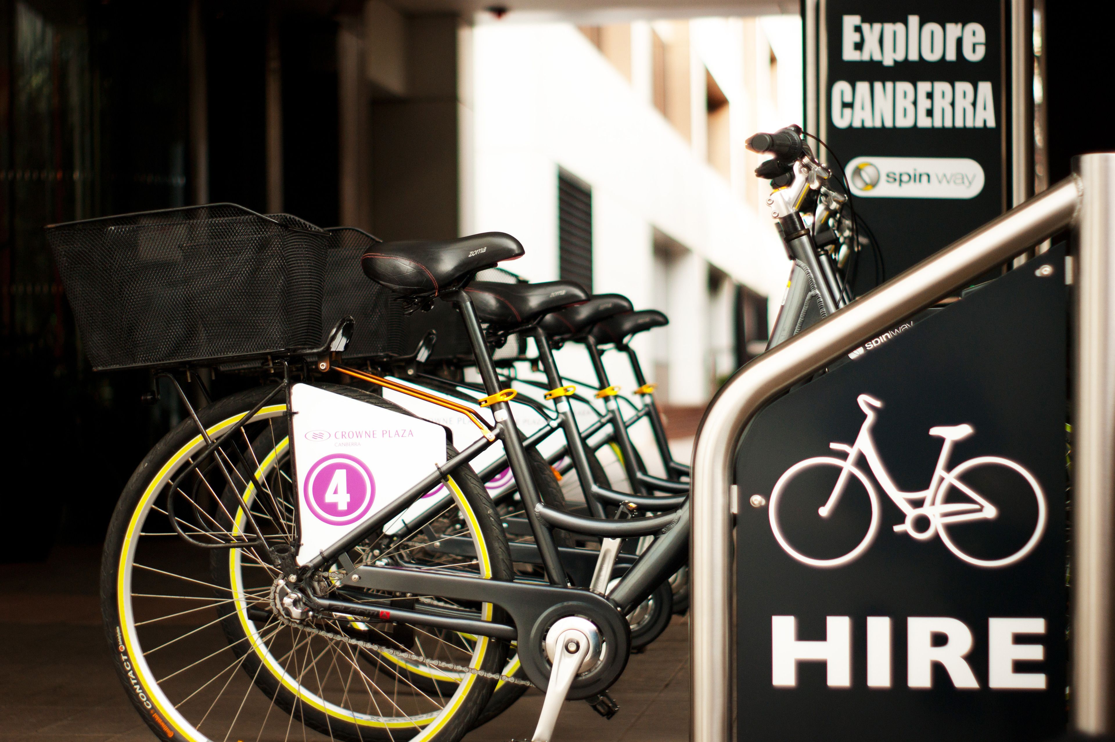 Una hilera de bicicletas con un cartel de 'HIRE' y el logotipo de 'spin way', indicando un servicio de alquiler de bicicletas.