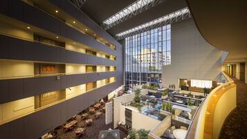 A multi-level hotel lobby with a central atrium, multiple dining areas, and a glass facade offering views of the city.