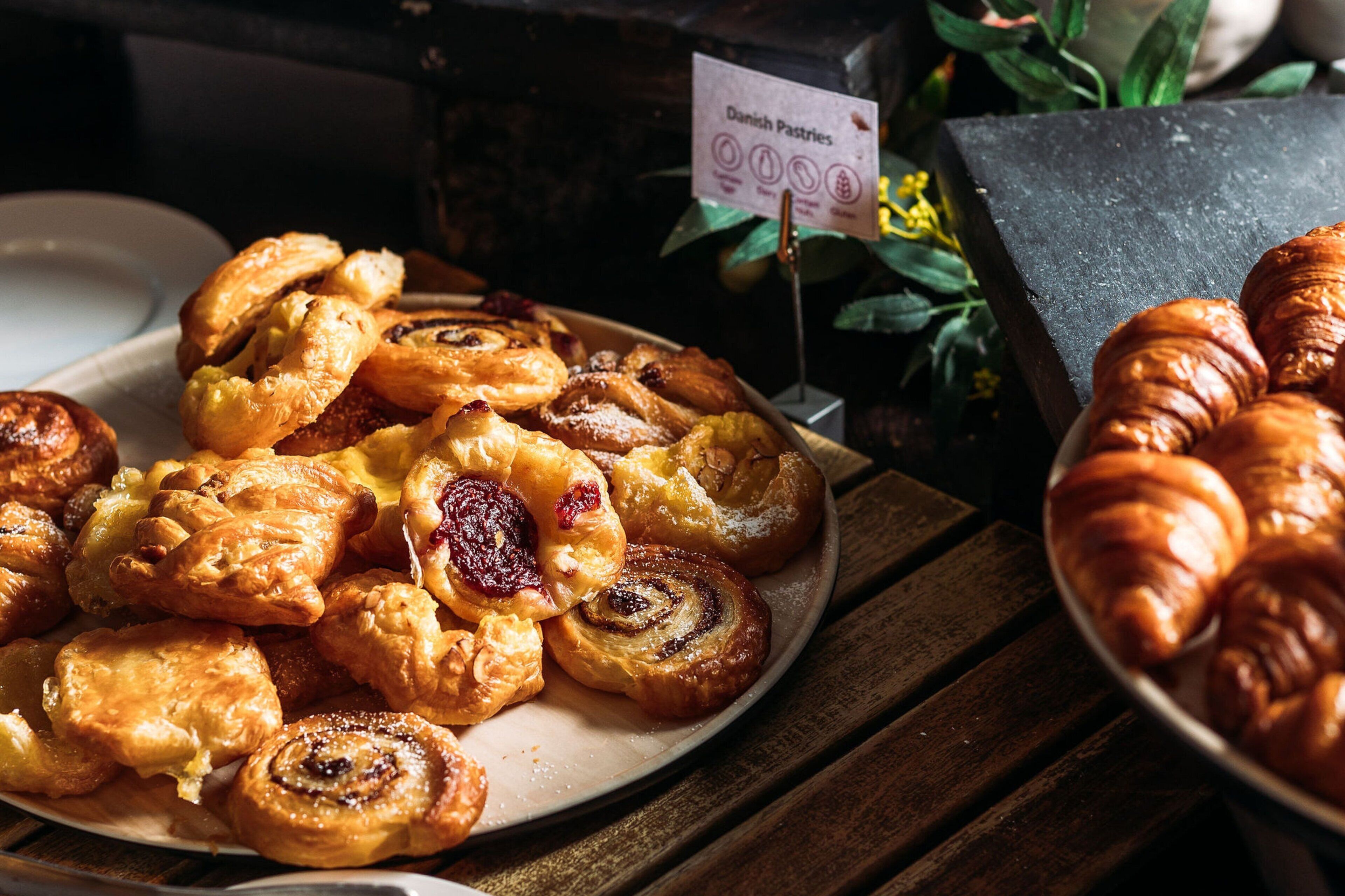A variety of pastries on a plate, including croissants and cinnamon rolls, with a sign indicating 'Danish Pastries'.