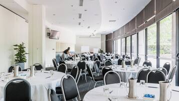 Uma sala de conferência com mesas redondas, cadeiras e um quadro branco.