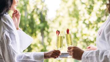 Deux personnes trinquent avec des coupes de champagne, chacune étant décorée d’une fraise, dans une pièce dont la fenêtre donne sur un paysage verdoyant.