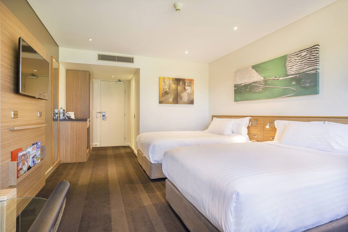 Una habitación de hotel con dos camas, un escritorio de madera, un espejo y obras de arte en la pared.
