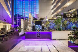 Un vestíbulo de hotel con recepción, zona de bar y área de descanso con mesas y sillas.