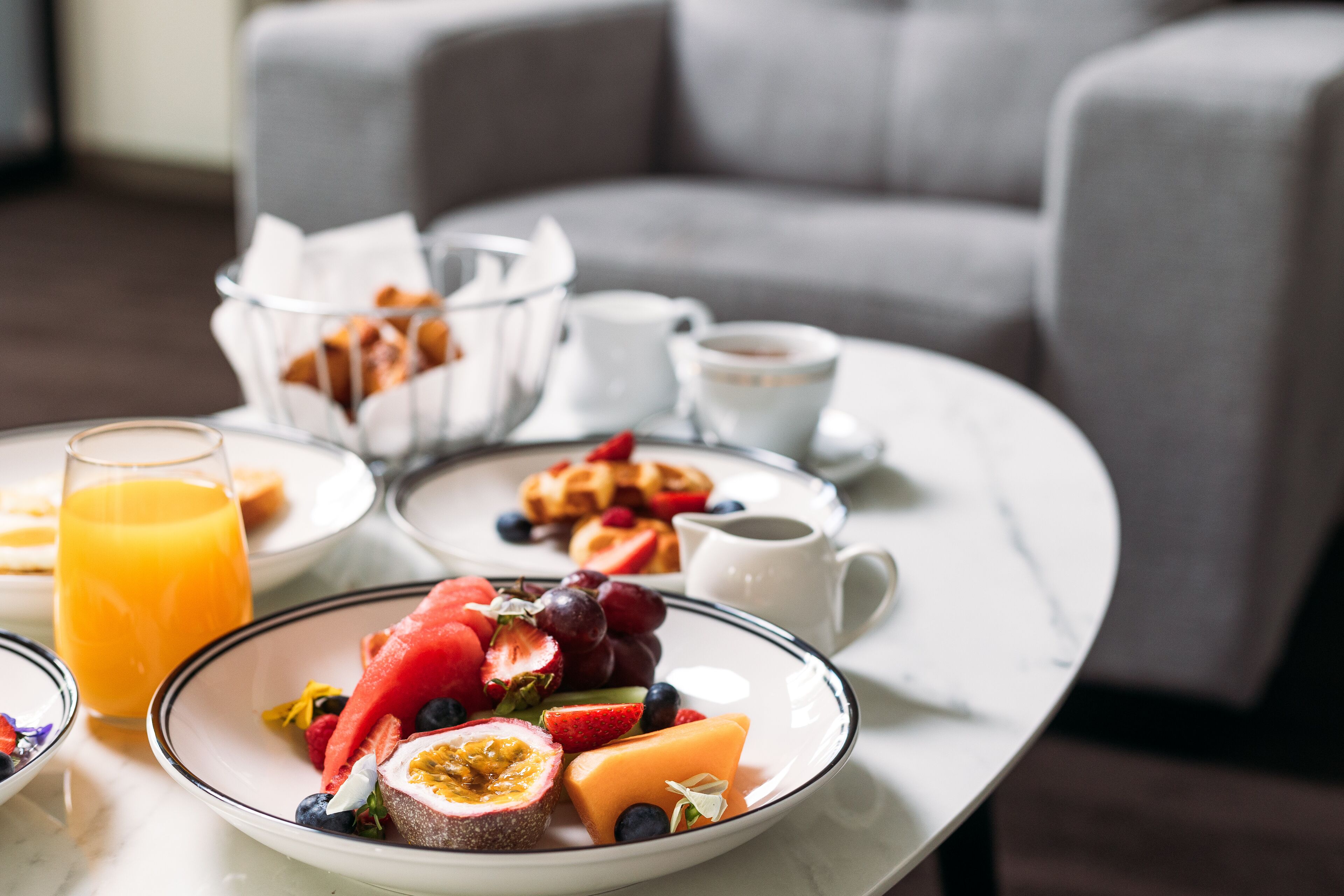 A breakfast setting with a variety of fruits and pastries on a table, a coffee cup, and a glass of orange juice.