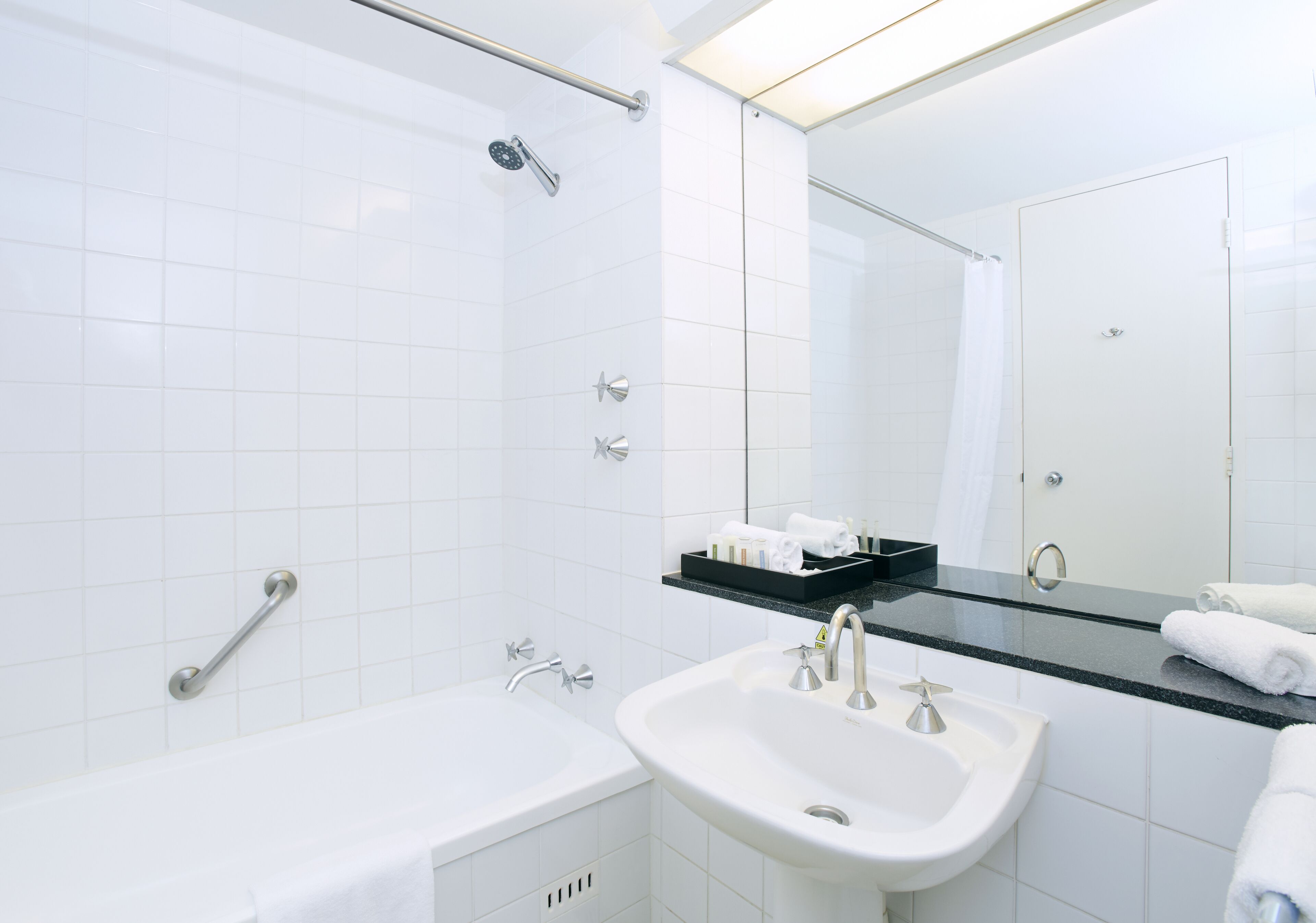 A modern bathroom with a bathtub, a sink, and a shower. There is a mirror above the sink and a towel rack beside it.