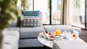 A modern living room with a grey sofa, patterned cushions, a round coffee table with breakfast items, and a view of the outdoors through large windows. - Crowne Plaza Canberra by IHG (Canberra)