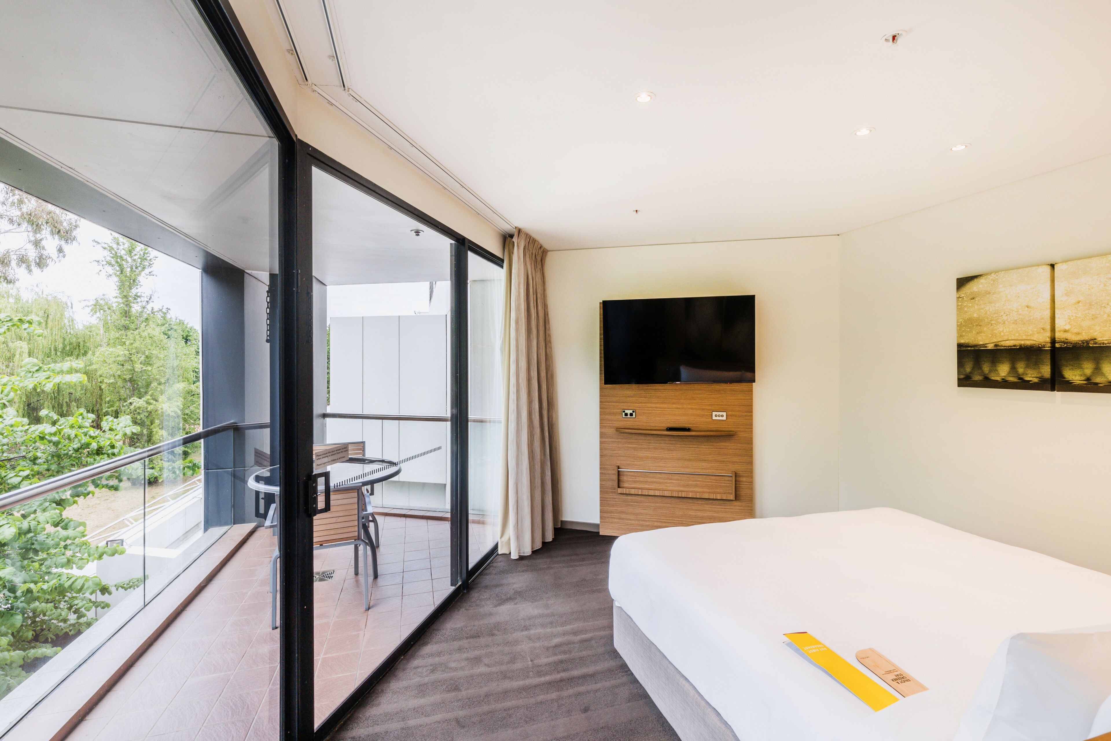 Una camera d'albergo con balcone, un letto, una televisione e un armadio in legno.