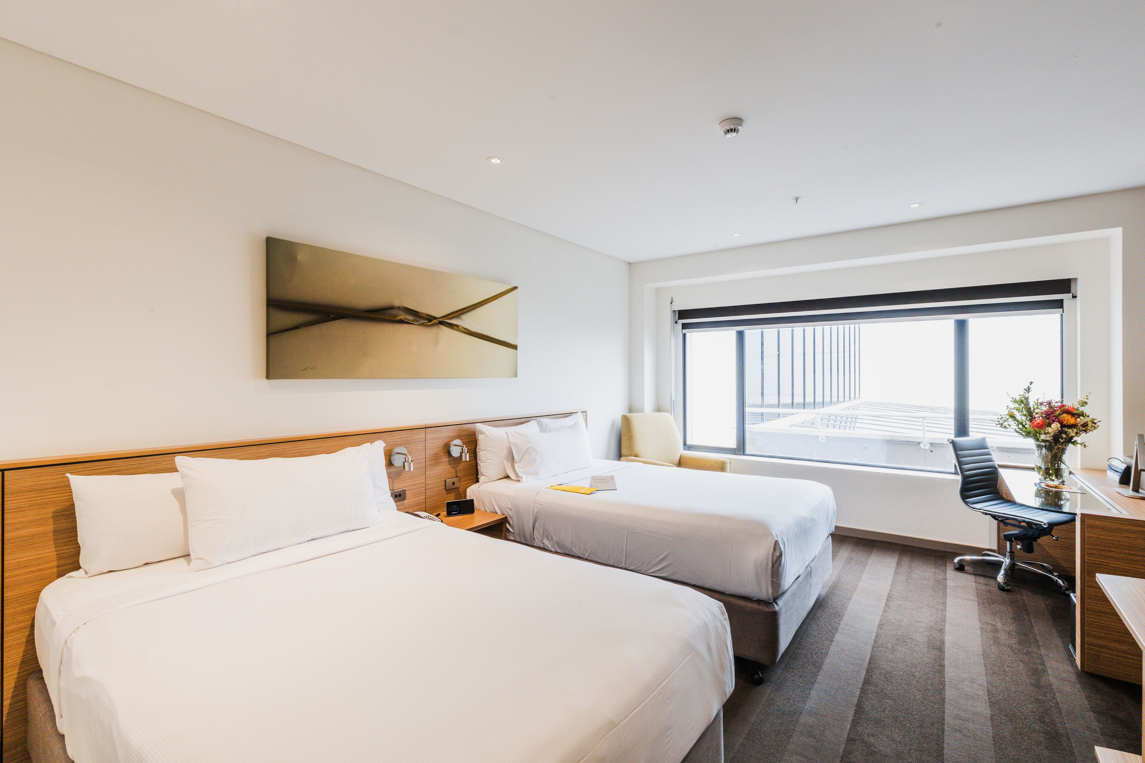 Habitación de hotel con dos camas, un escritorio y un ventanal grande.