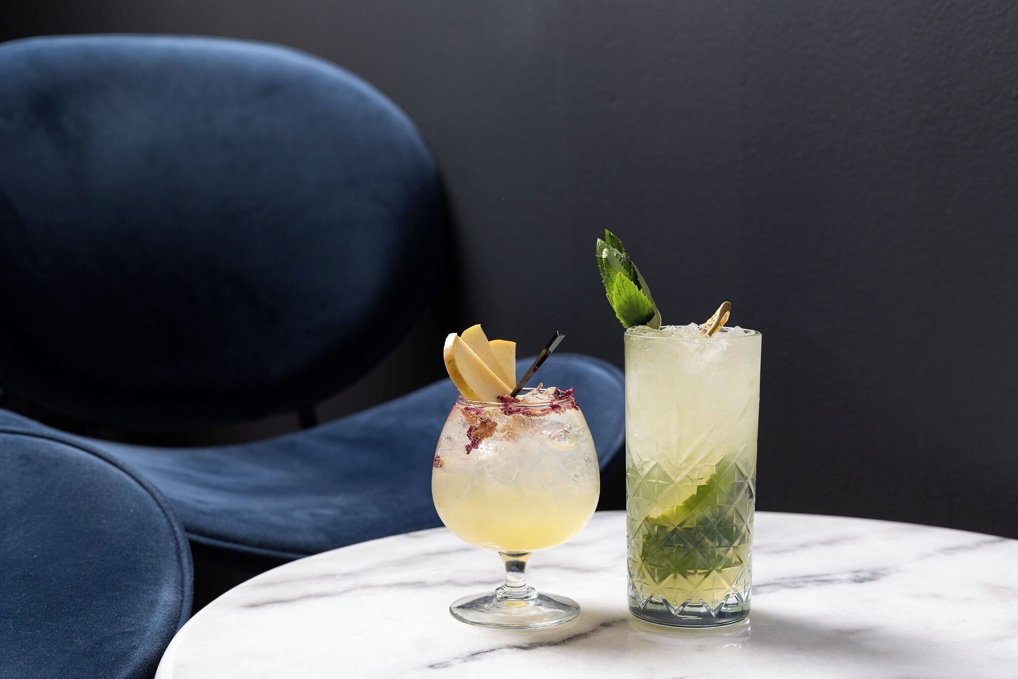 Two drinks on a marble table with a dark blue chair in the background.