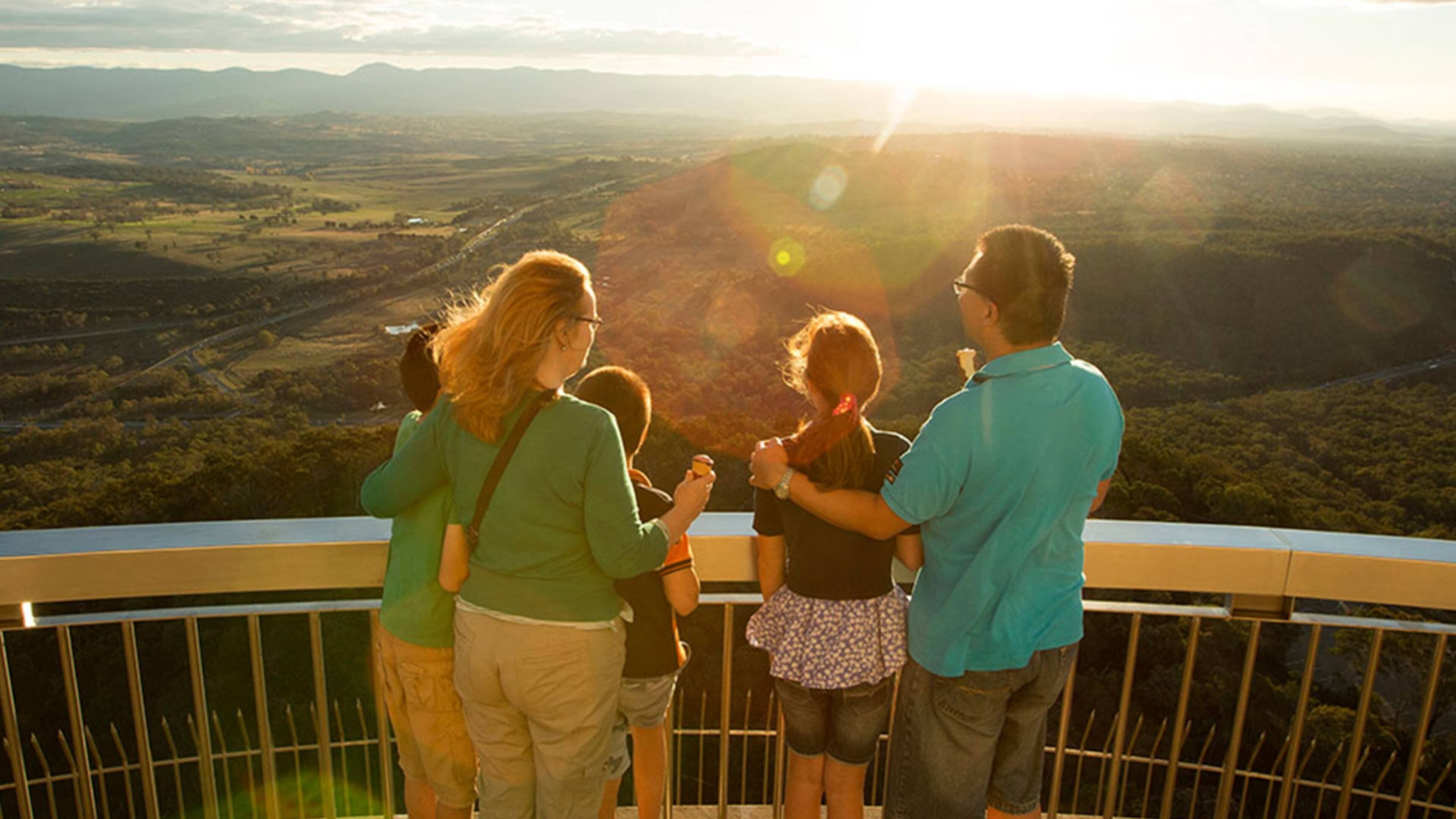 A group of people standing on a balcony overlooking a valley with a sunset in the background.