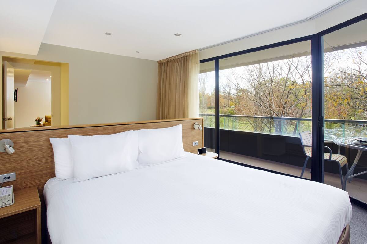 Una habitación de hotel moderna con una cama grande, una mesita de noche con teléfono y un balcón con mesa y sillas.