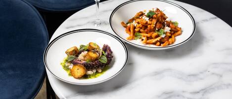 Two bowls of pasta on a white marble table with a glass of white wine.