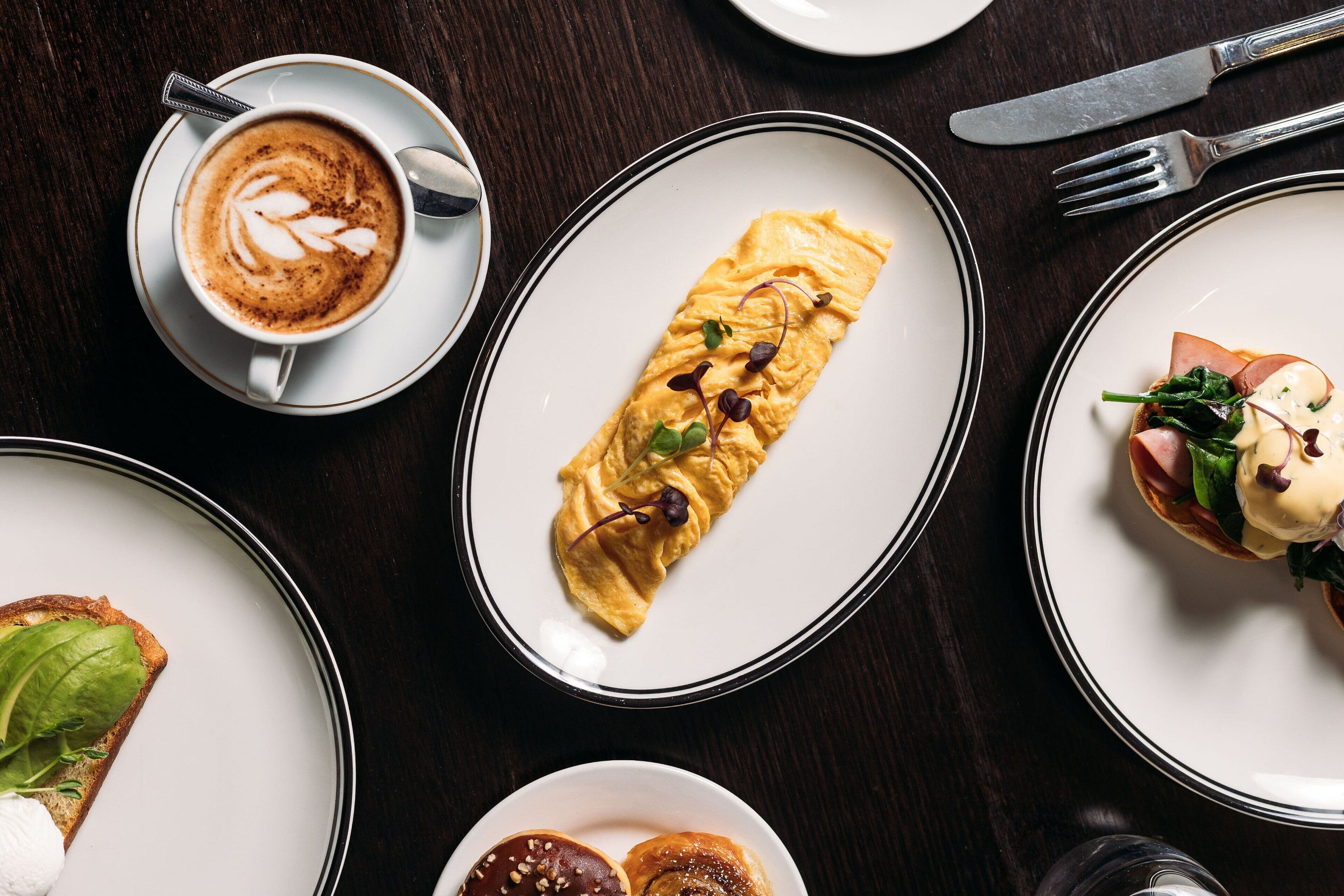 A variety of dishes on plates, including an omelette, a sandwich, and a cup of coffee.