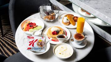 A breakfast tray with pancakes, fruit, yogurt, and a juice glass on a marble table.