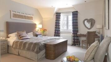 A bedroom with a bed, bedside table, lamp, window with curtains, chair, and a small table with fruit.