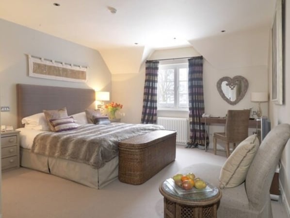 A bedroom with a bed, bedside table, lamp, window with curtains, chair, and a small table with fruit.