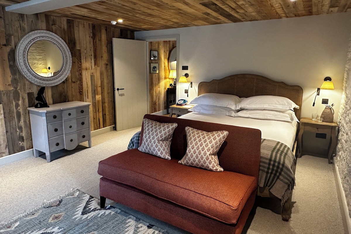 Une chambre avec un plafond en bois, un lit recouvert de draps blancs, un banc rouge et une table de chevet avec une lampe.