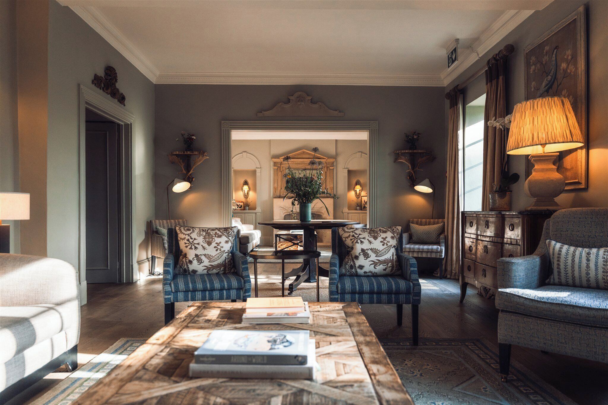 A living room with a coffee table, two armchairs, a sofa, a mirror, and a lamp.