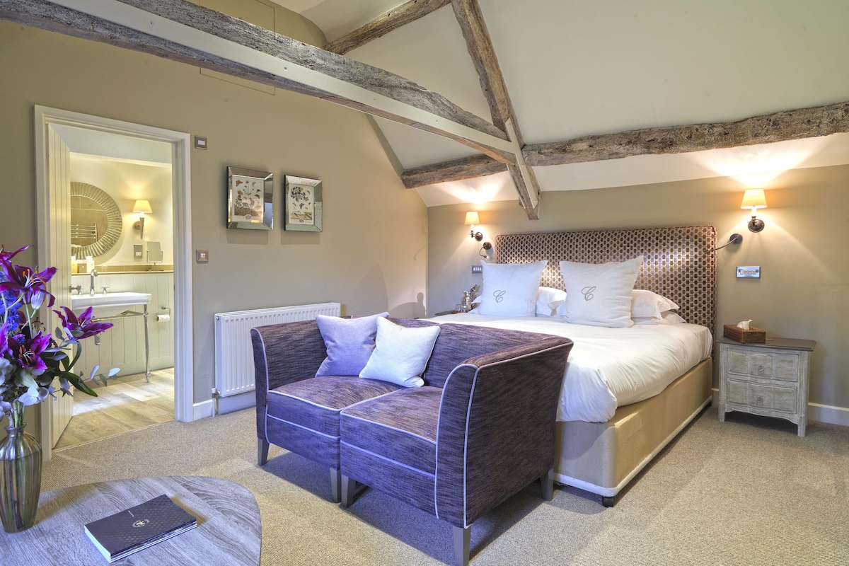 Une chambre avec un grand lit, un canapé, une table de chevet, une commode, un radiateur, un miroir et un vase avec des fleurs.