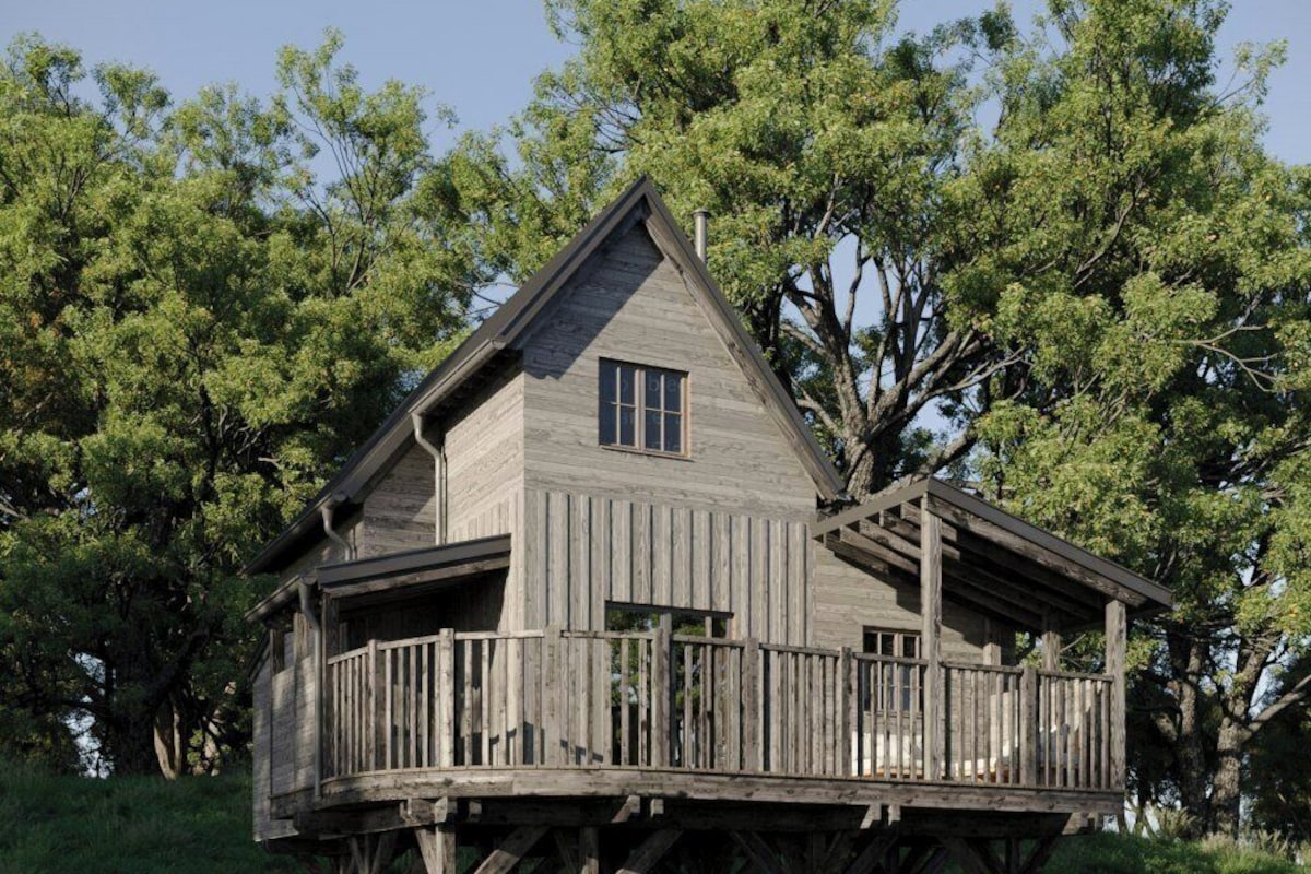Une maison en bois dotée d’un balcon sur pilotis, entourée d’arbres.