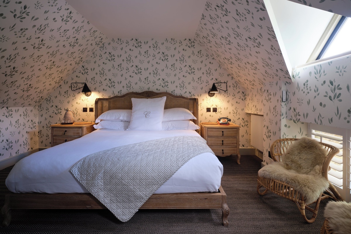 Une chambre à coucher avec un lit, des tables de chevet, une chaise et une lucarne.