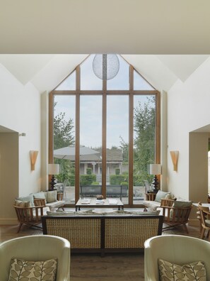 A spacious room with large windows, a central seating area with a table, and two chairs.