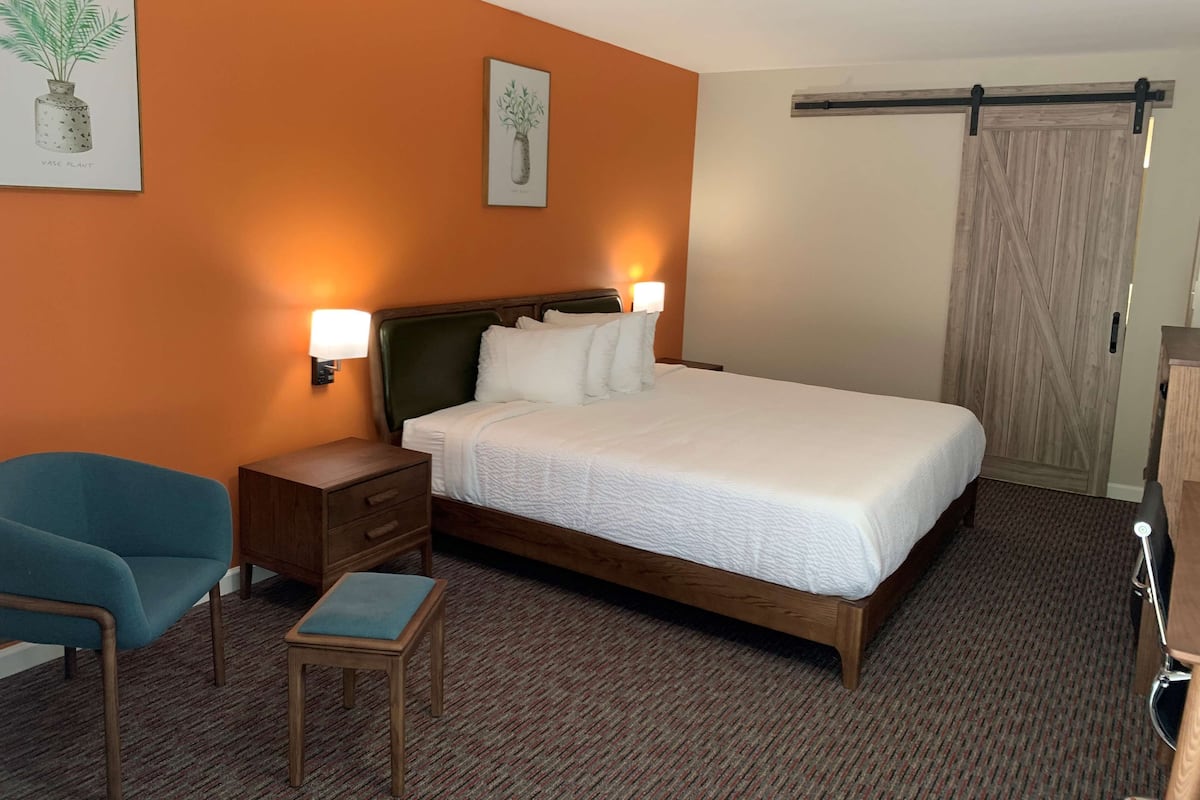 Een hotelkamer met een bed, nachtkastjes, een stoel, een klein tafeltje en kunstwerken aan de muren.