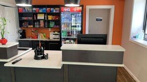 Un espace d’accueil comprenant un comptoir, un réfrigérateur rempli de boissons, une machine à café et une étagère avec des en-cas.