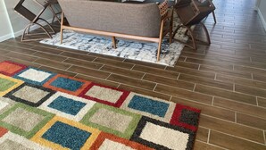 Un salon avec un canapé, des fauteuils, un téléviseur et un tapis à motifs.