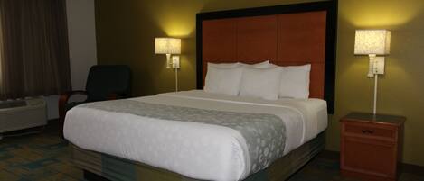 A hotel room with a large bed, two bedside lamps, a chair, and a heater.